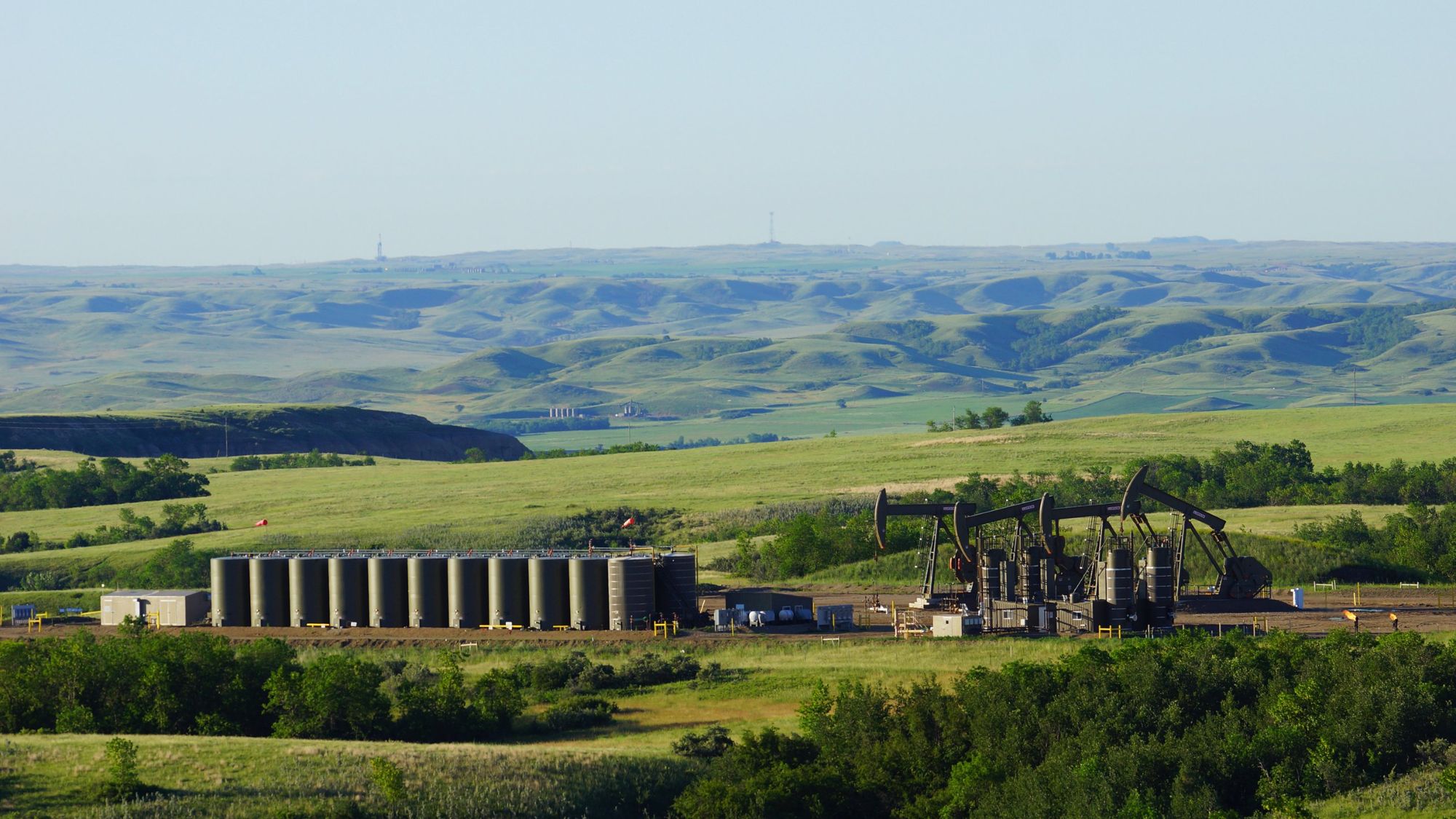 Tank battery and pumpjacks among rolling green hills